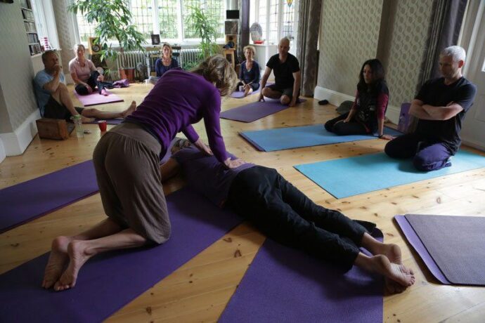 People gathered around looking at a student on the floor in an online yoga workshop class at erling.yoga