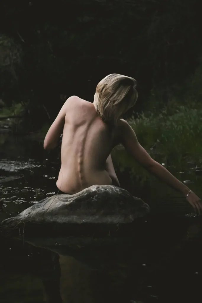 woman sat on rock in stream showing her spine side bending for an article on yoga poses