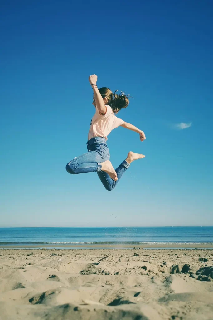 girl jumping in the air on a beach for a blog on yoga poses